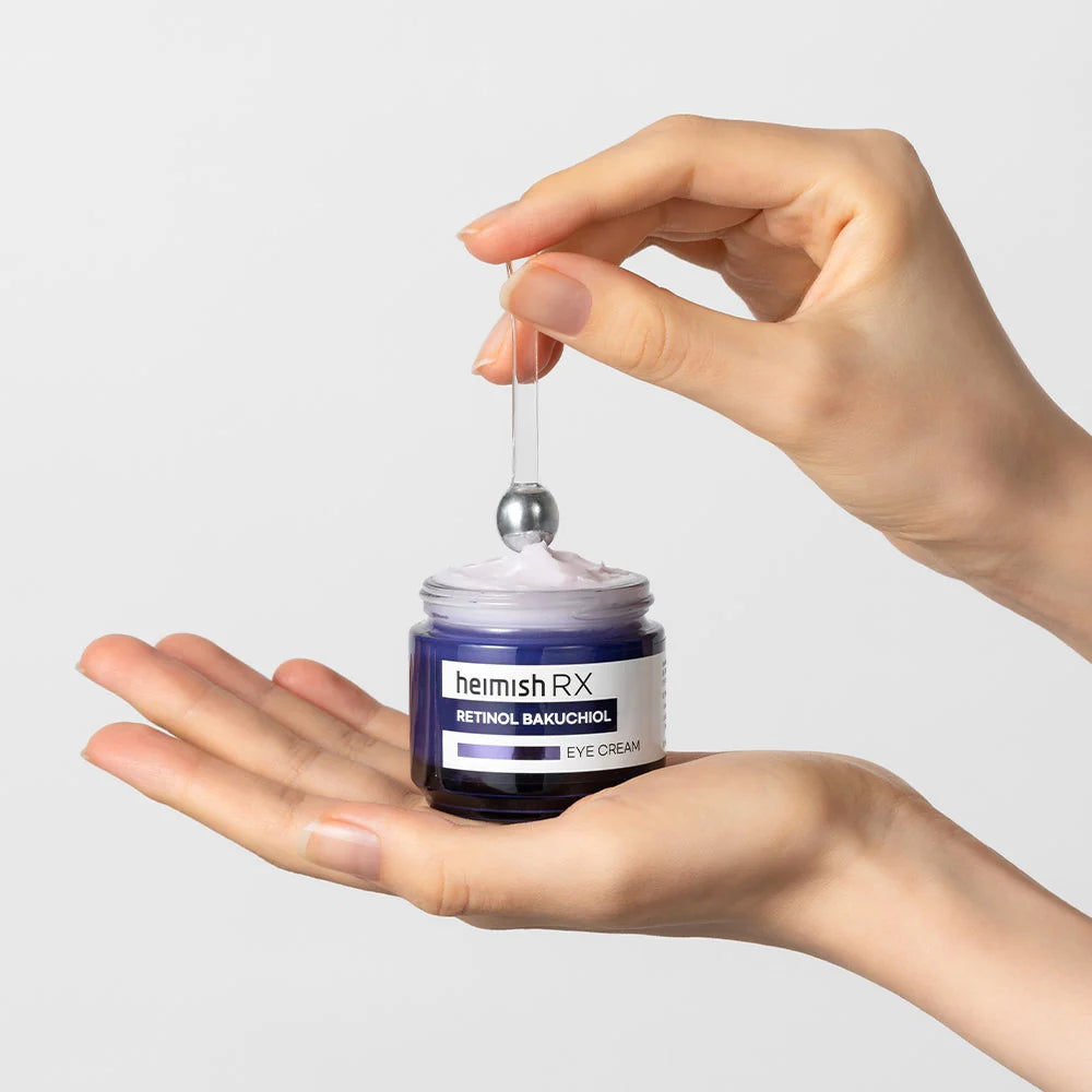Mão a segurar o Heimish RX Retinol Bakuchiol Eye Cream aberto, aplicador metálico sobre o creme