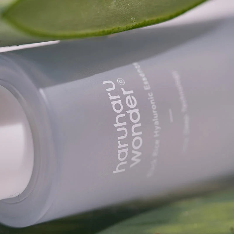 Frasco Haruharu Wonder Black Rice Hyaluronic Essence em plano aproximado, com folha de aloé vera ao fundo