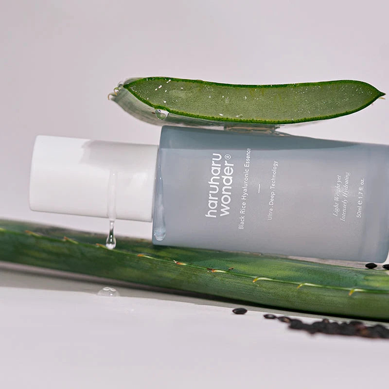 Frasco Haruharu Wonder Black Rice Hyaluronic Essence deitado, com gel a escorrer e grãos de arroz preto