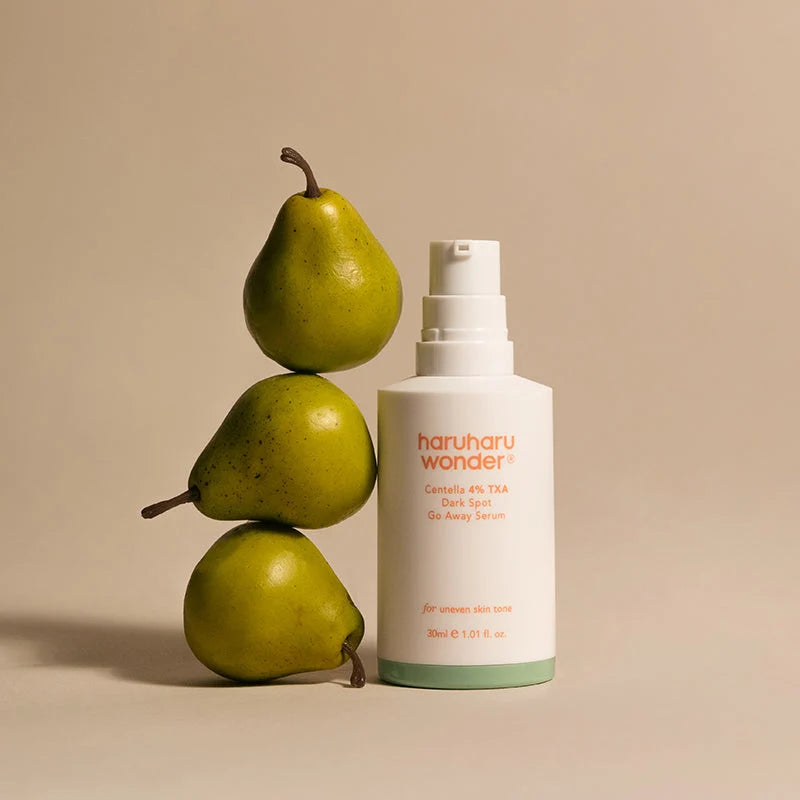 Frasco do sérum Haruharu Wonder Centella TXA junto a peras empilhadas, fundo bege