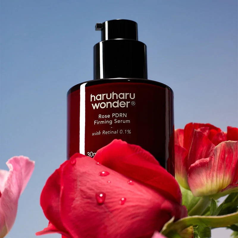 Frasco com doseador do Rose PDRN Firming Serum rodeado por rosas vermelhas ao ar livre
