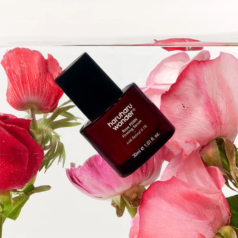 Rose PDRN Firming Serum submerso em água, entre pétalas de rosa vermelhas e cor-de-rosa