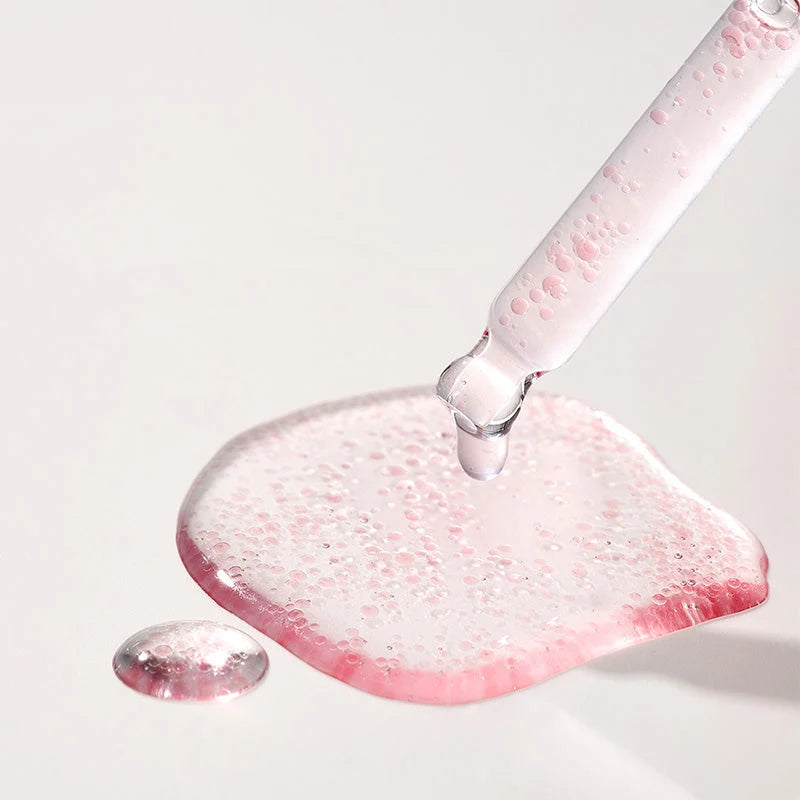 Gota de fórmula rosa com pequenas cápsulas sobre o conta-gotas de vidro, em fundo claro