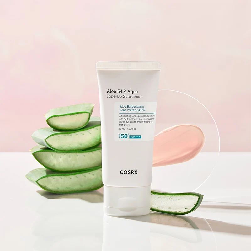 COSRX Aloe 54.2 Aqua Tone-Up Sunscreen junto a folhas de aloé vera frescas sobre fundo rosa