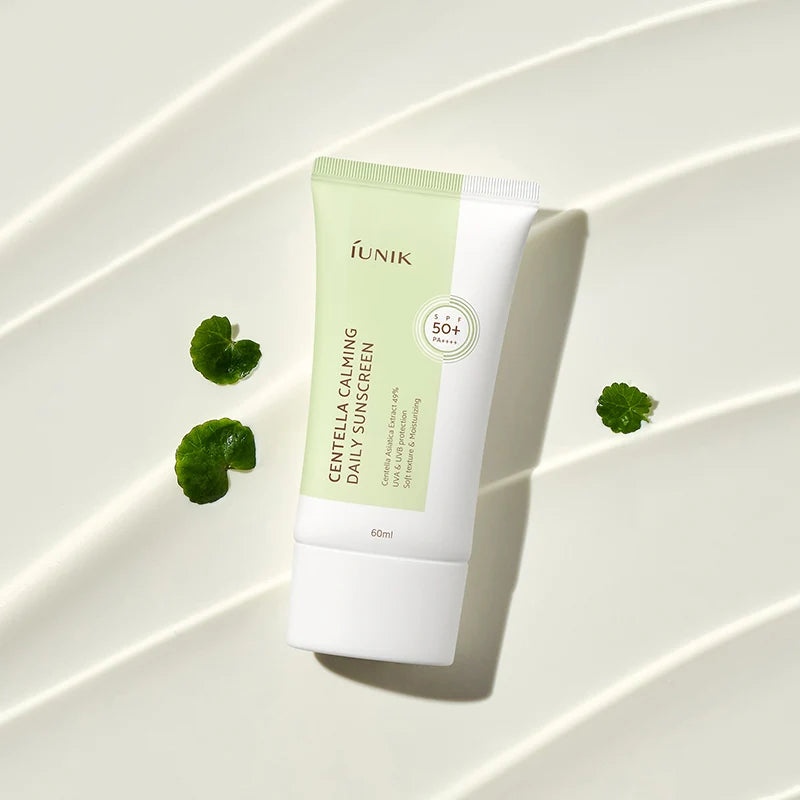 Tubo IUNIK Centella Calming Daily Sunscreen junto a folhas de centella asiática sobre fundo texturado