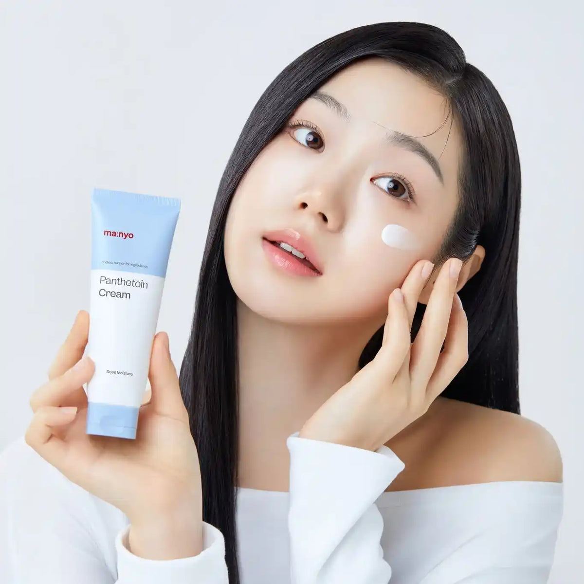 Modelo segura o ma:nyo Panthetoin Cream com uma porção de creme aplicada na face