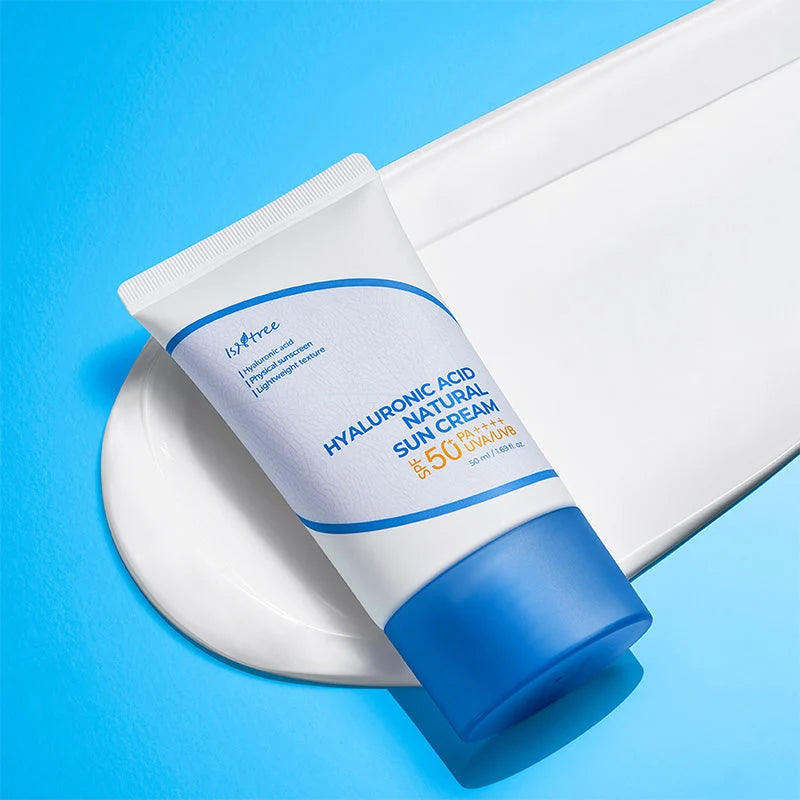Isntree Hyaluronic Acid Natural Sun Cream deitado sobre superfície branca curva, com fundo azul