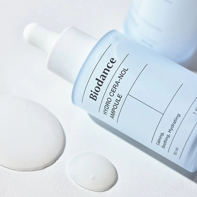 Biodance Hydro Cera-Nol Ampoule deitada com gotas de textura aquosa ao lado
