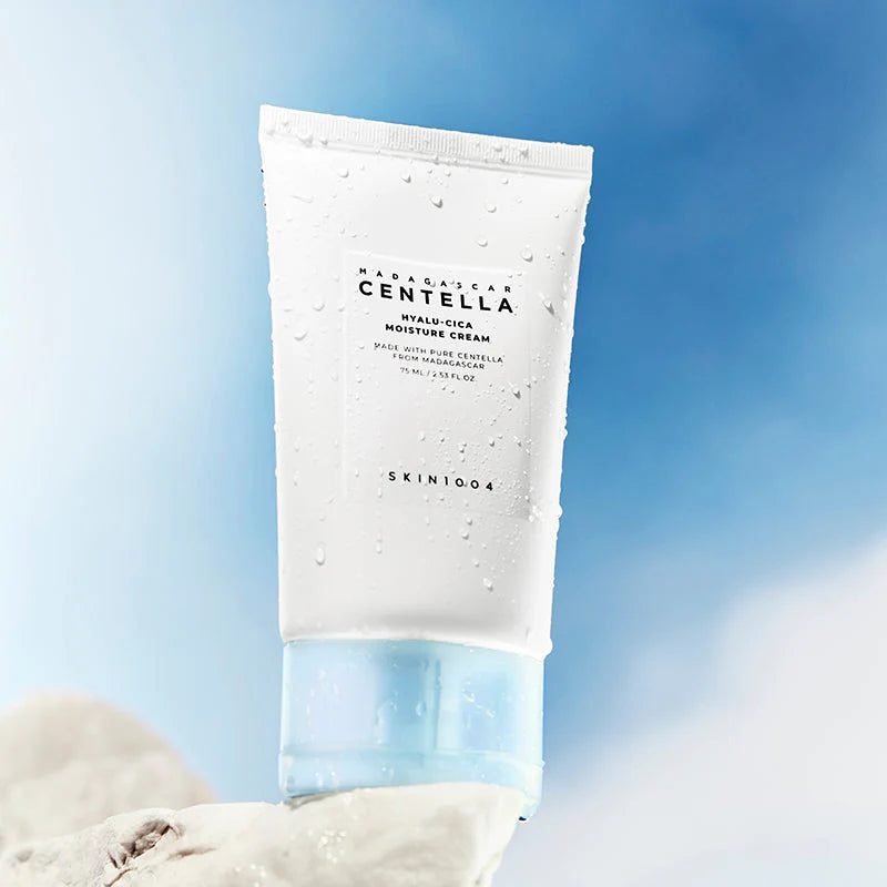 SKIN1004 Hyalu-Cica Moisture Cream tube com gotas de água sobre pedra, fundo céu azul