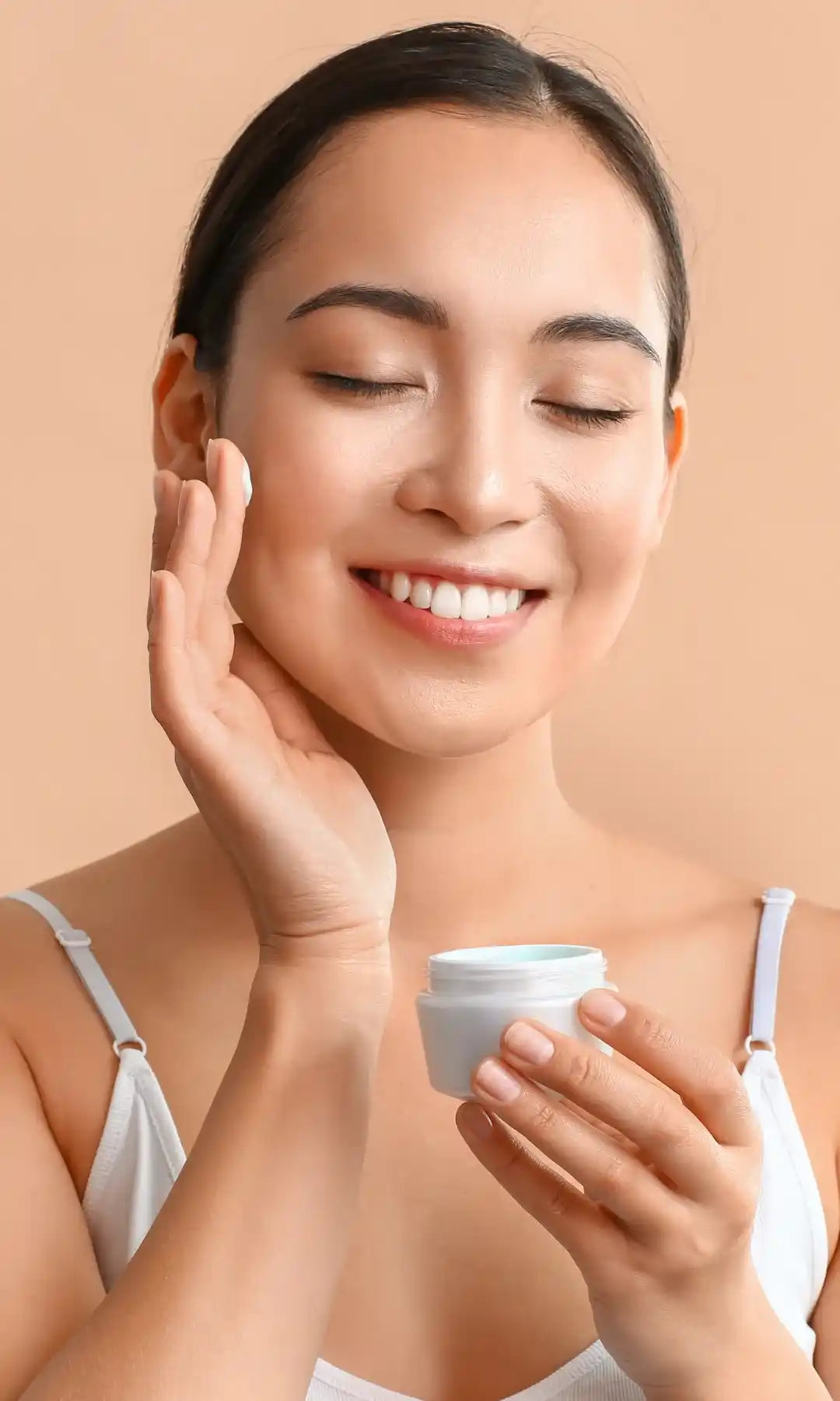 Mulher a aplicar creme hidratante no rosto, sorrindo — categoria de produtos para pele seca