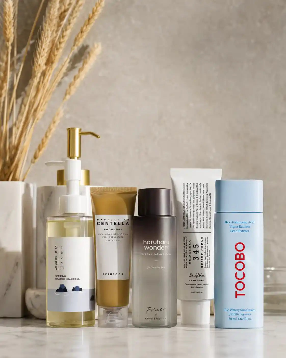Rotina de skincare com 5 produtos numerados: óleo de limpeza Round Lab, espuma Madagascar Centella, tónico Haruharu Wonder, creme Dr. Althea e protetor solar Tocobo